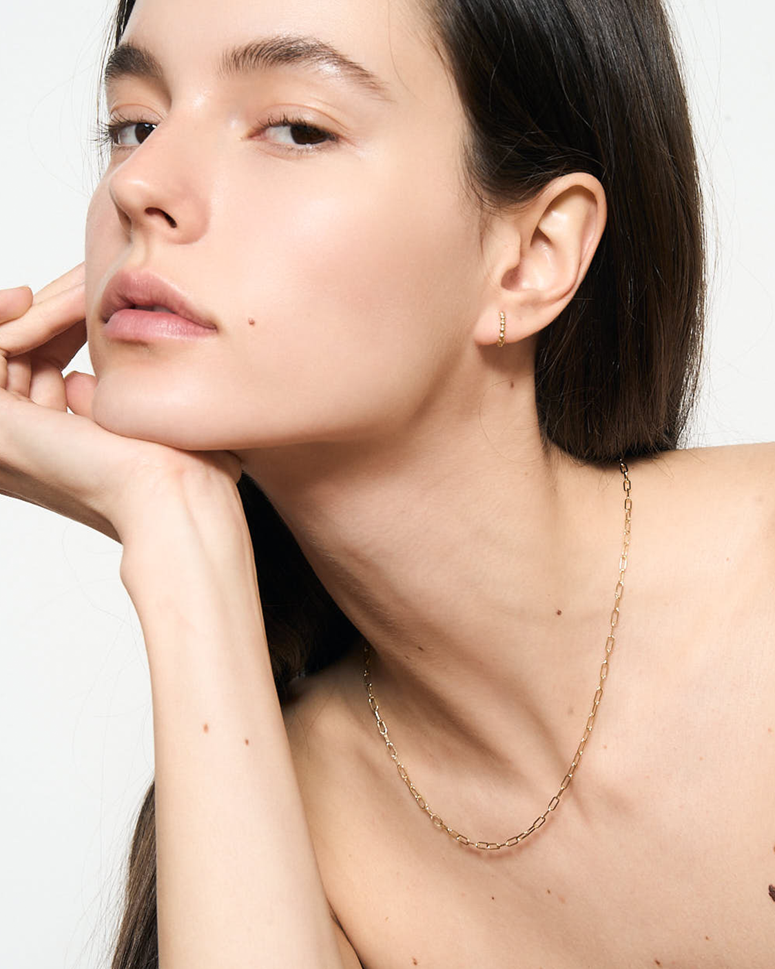 Close-up of a woman wearing a delicate gold necklace against a neutral background