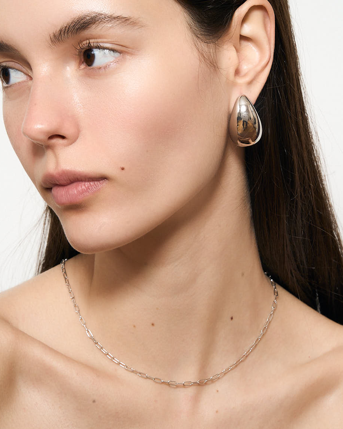 Close-up of a woman wearing silver hoop earrings and a delicate chain necklace.