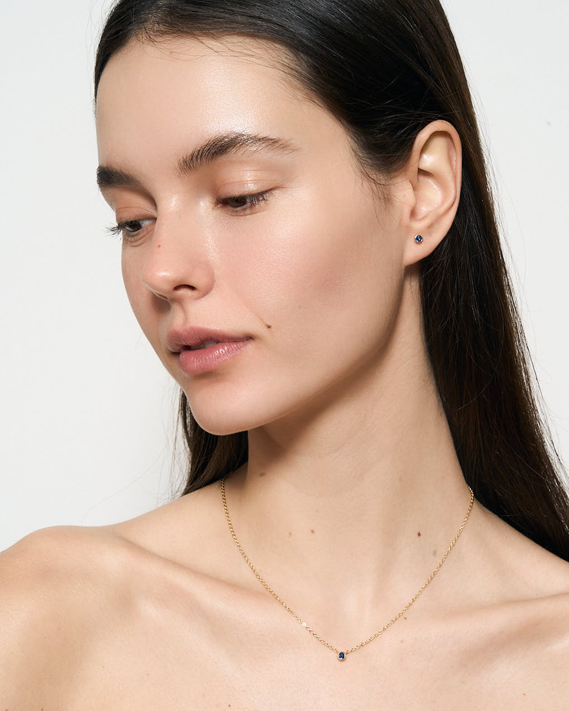 Woman wearing a gold necklace with small blue stones on a plain background