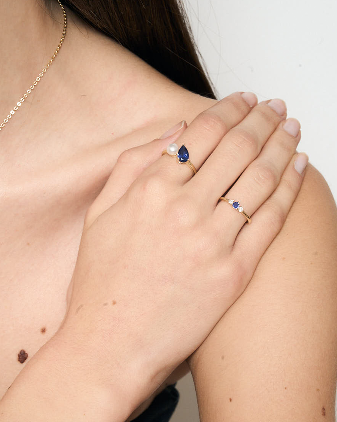 Close-up of a hand wearing two rings with blue gemstones on a neutral background