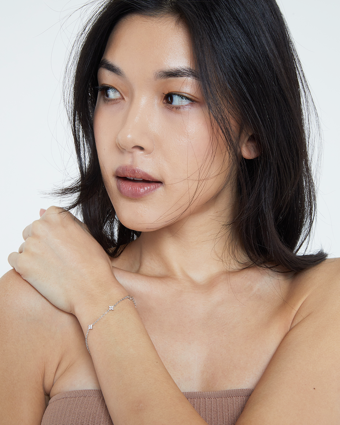 Woman wearing a delicate silver bracelet on a plain background