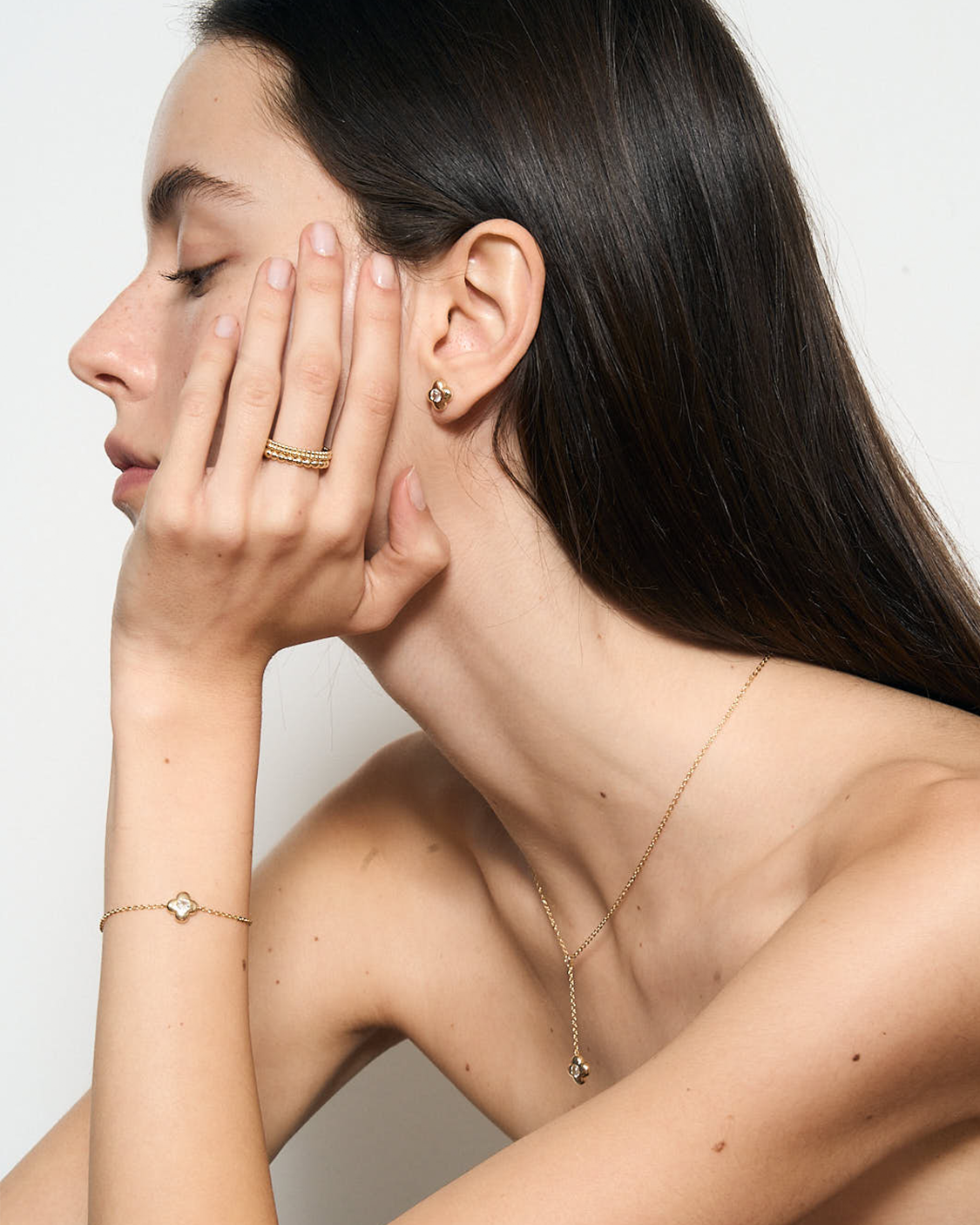 Woman wearing gold jewelry including earrings, necklace, and bracelet against a white background