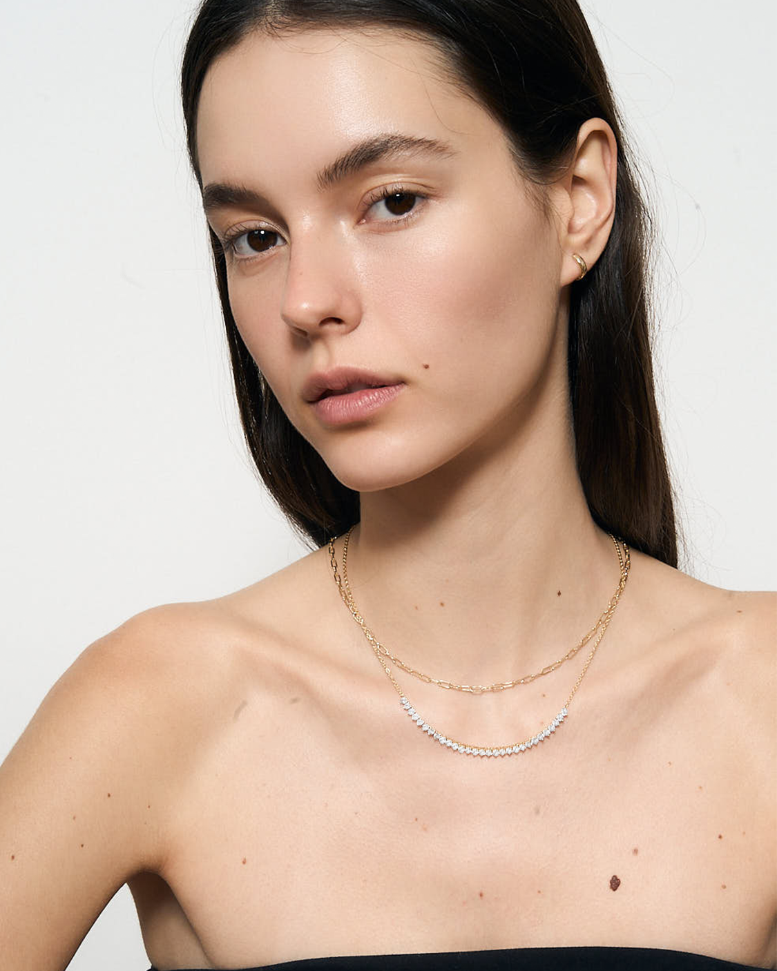 Woman wearing a delicate gold necklace on a plain background