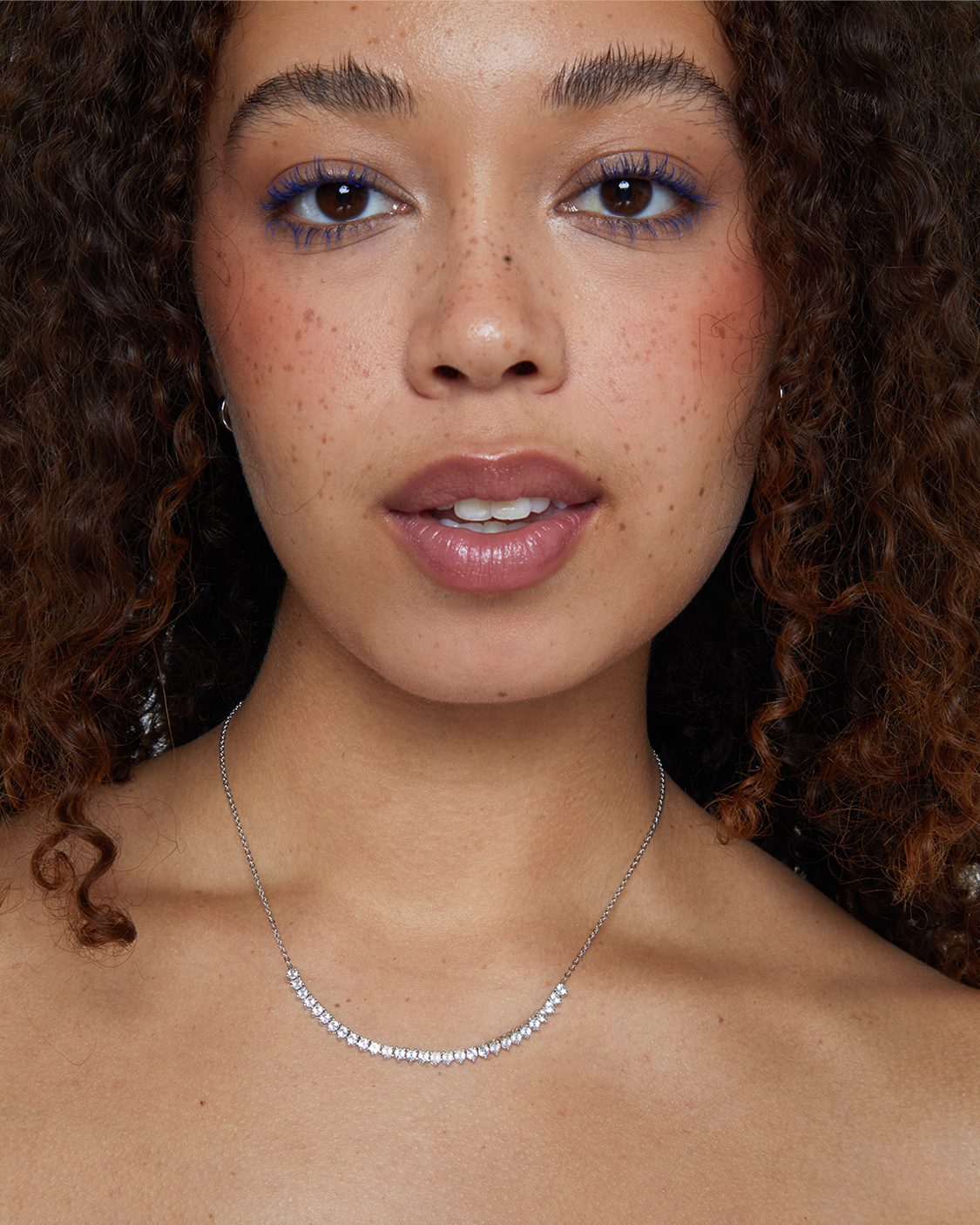 Close-up of a woman with curly hair wearing a silver necklace.
