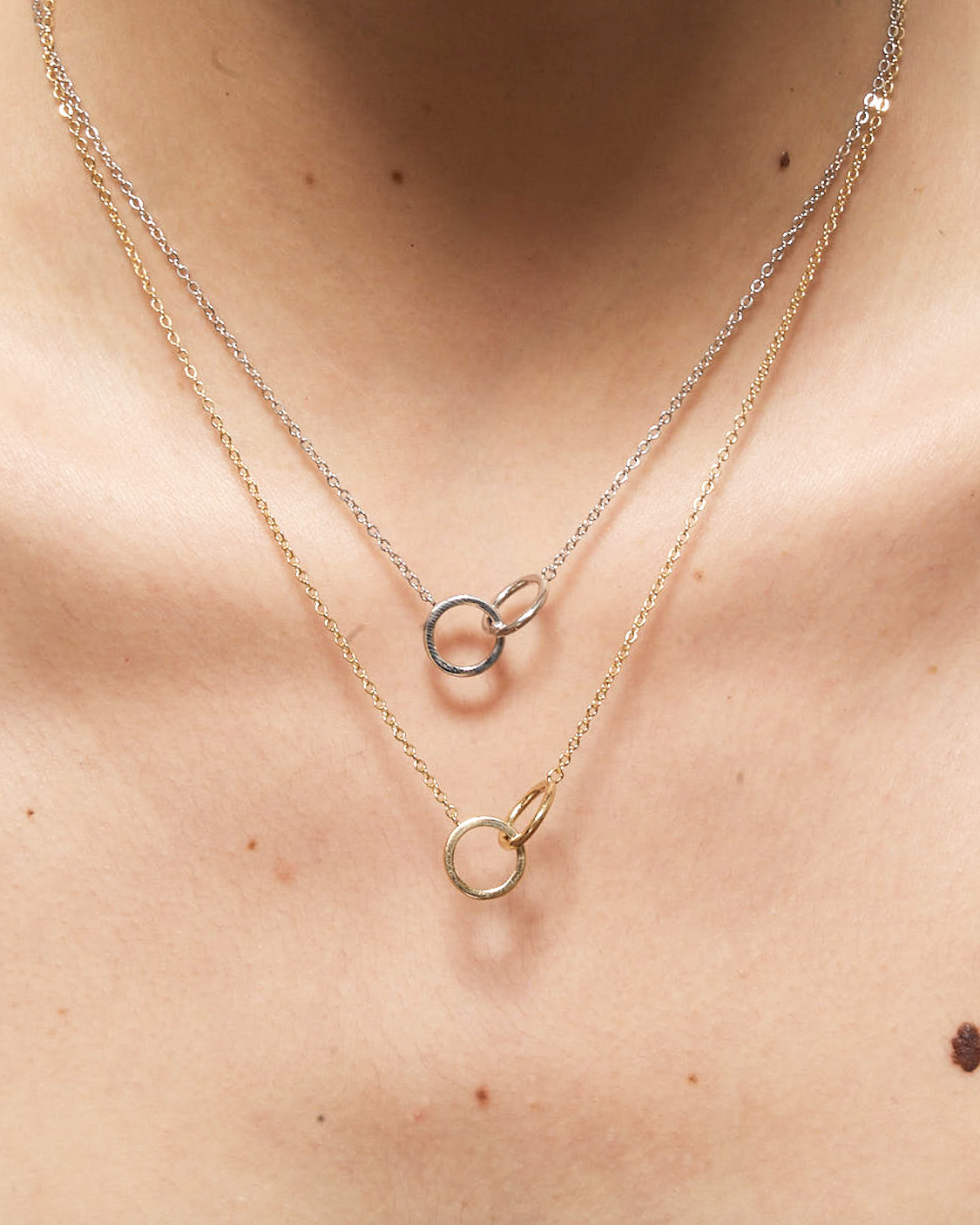 Two necklaces with circular pendants on a person's neck.