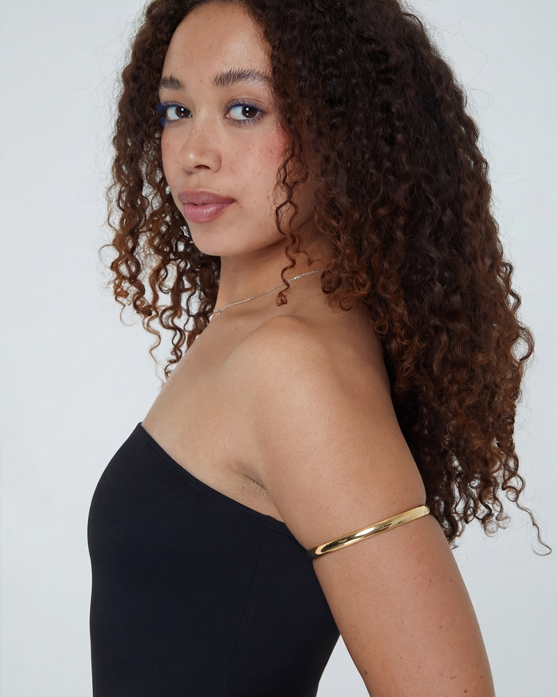 Woman with curly hair wearing a black strapless top and gold bracelet 