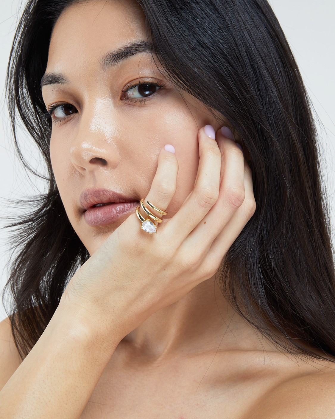 Woman with dark hair and gold rings on her fingers against a neutral background