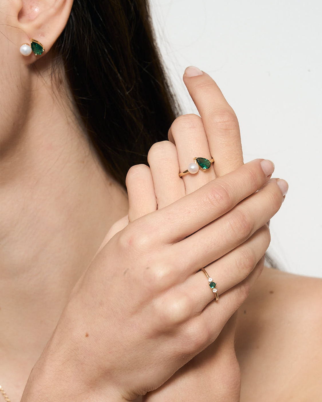 Close-up of a hand wearing a ring with a green gemstone and pearl, with matching earrings.