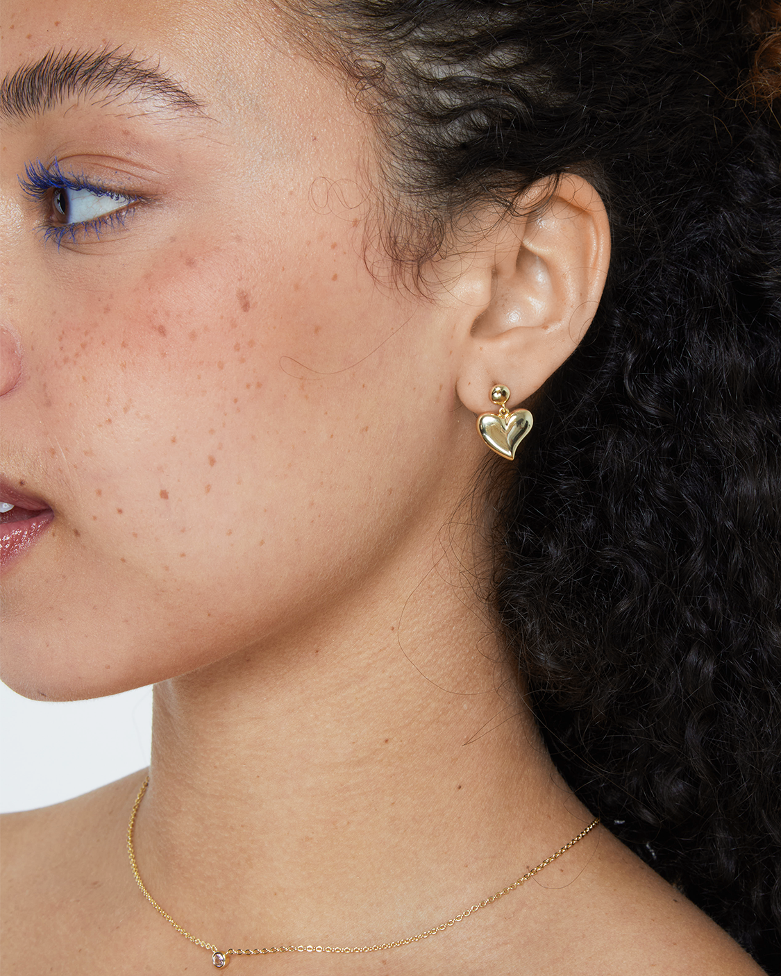 Close-up of a person wearing a gold heart-shaped earring and necklace.