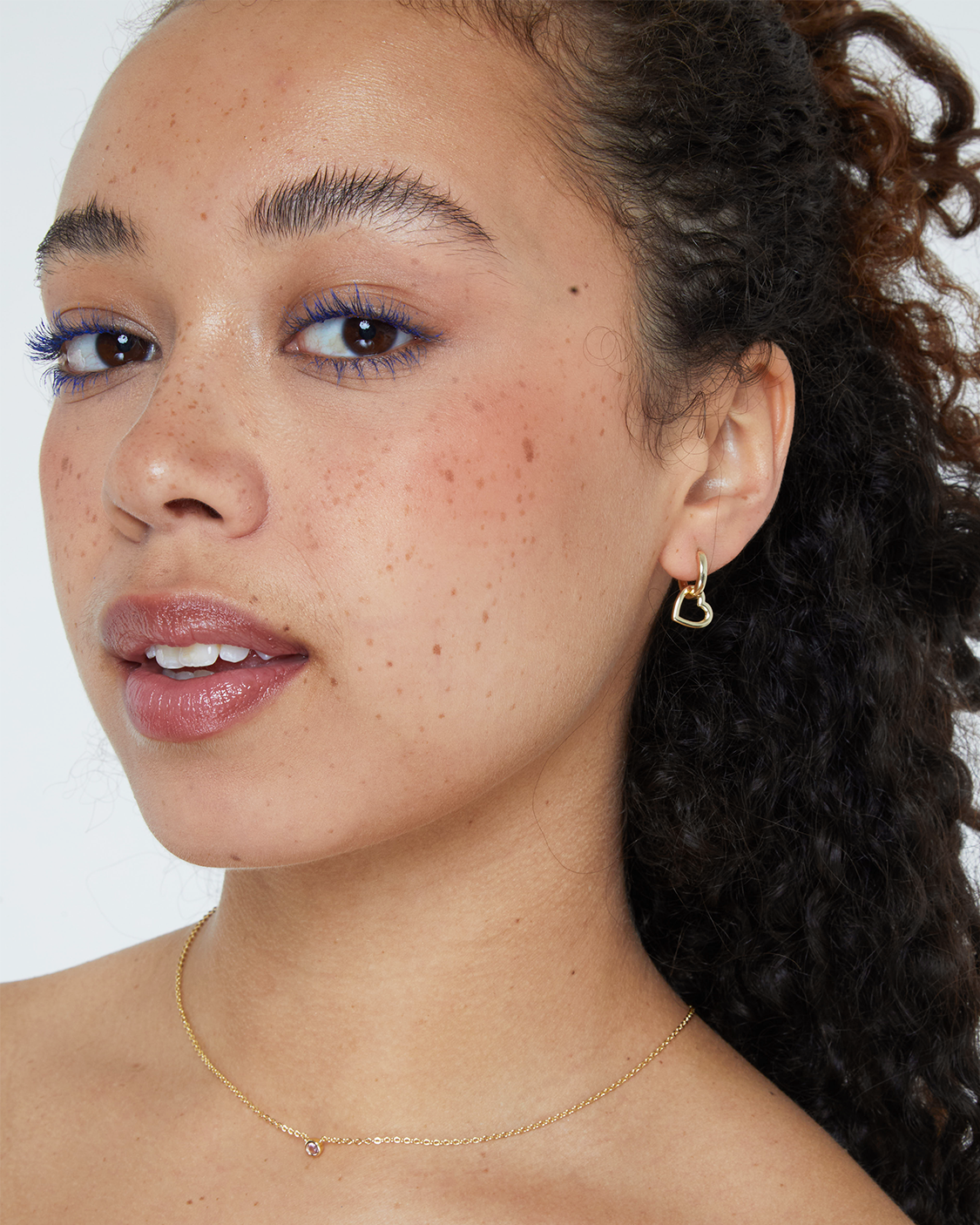 Close-up of a person with a gold earring and necklace on a white background