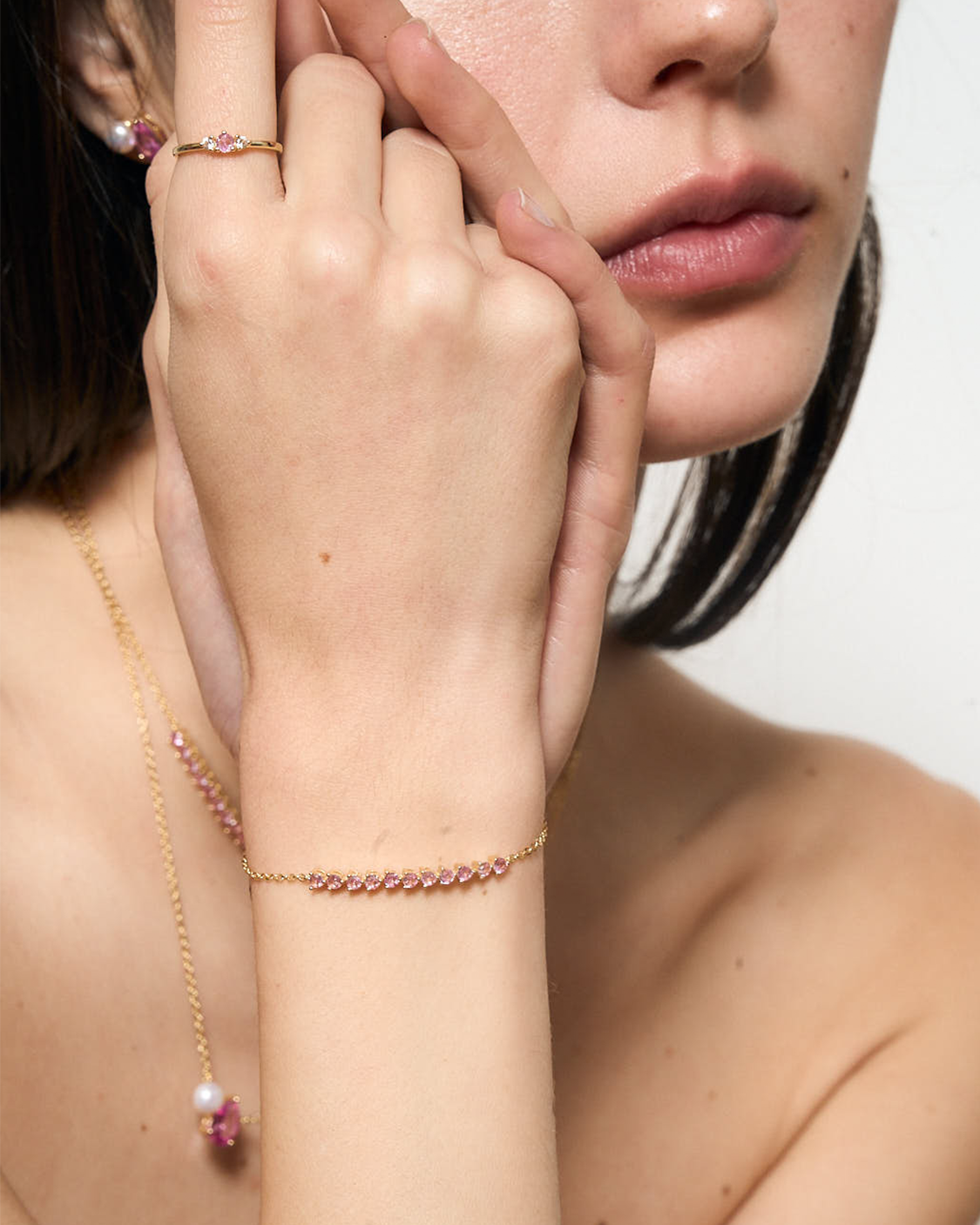 Close-up of a person wearing a gold bracelet with a pink gemstone on a neutral background