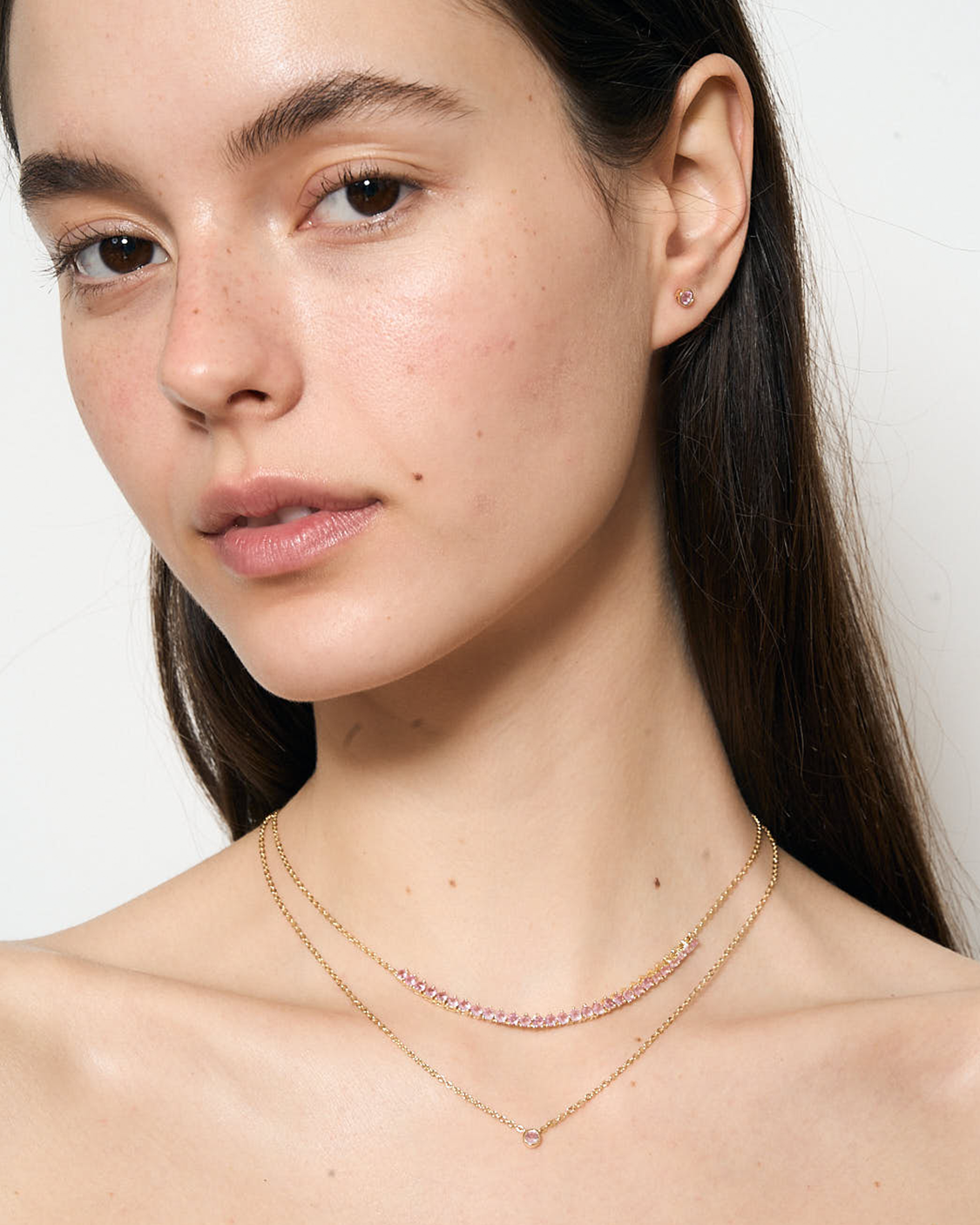 Close-up of a woman wearing two pink delicate necklaces against a plain background