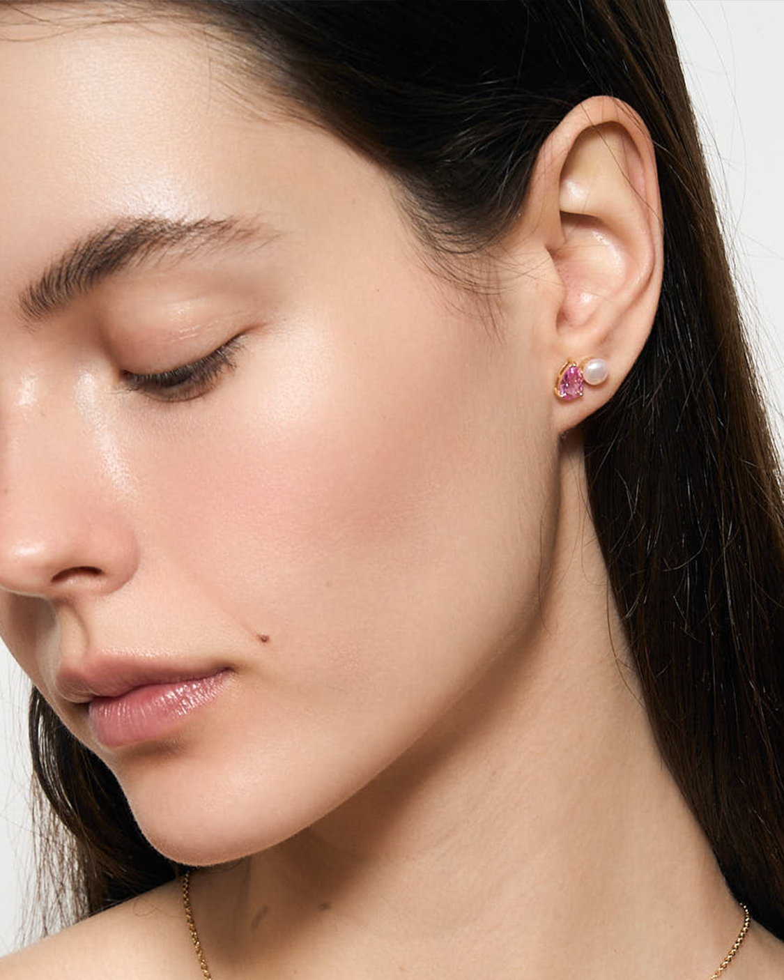 Close-up of a woman wearing pink gemstone earrings with a neutral background