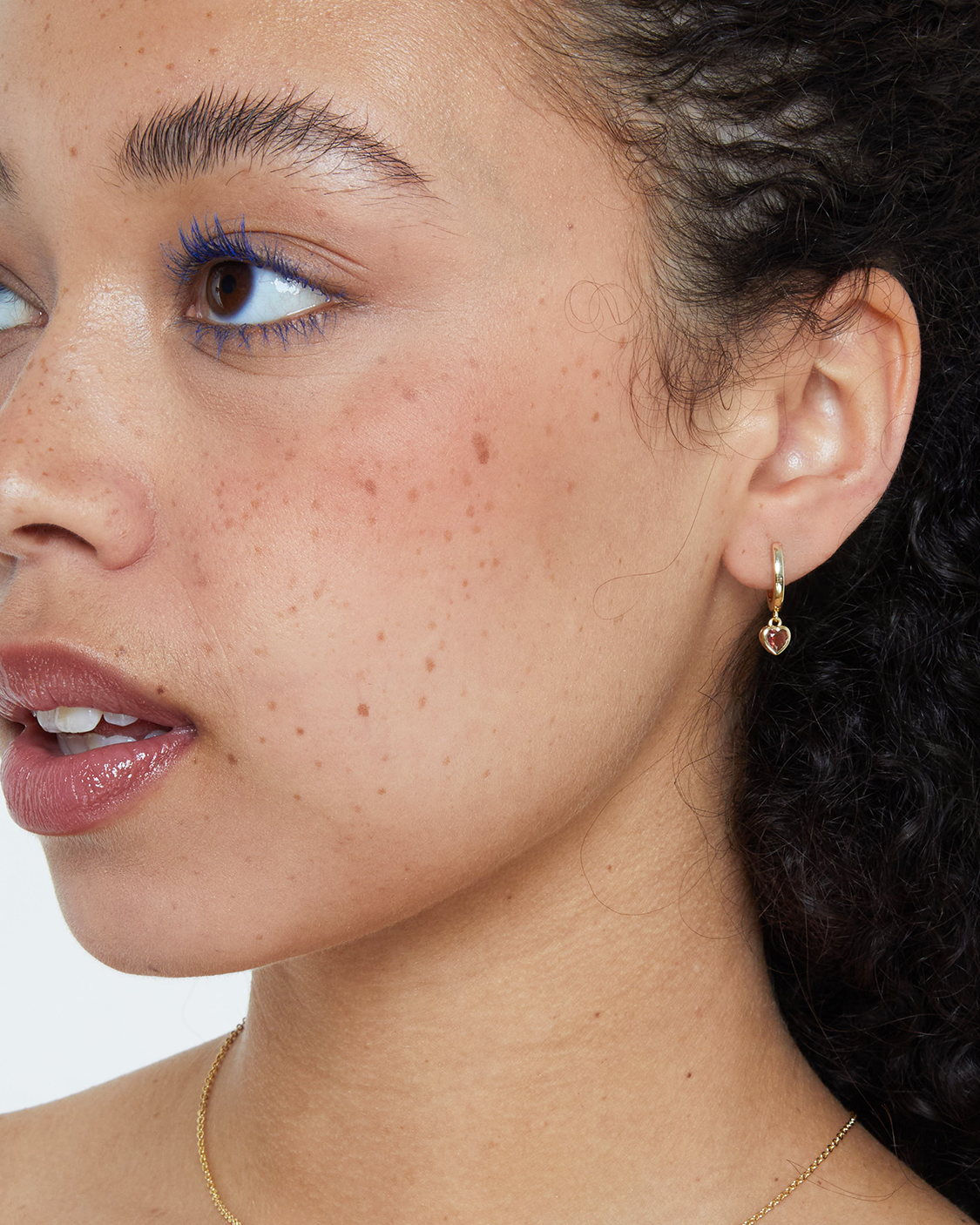 woman wearing gold huggie with red heart drop