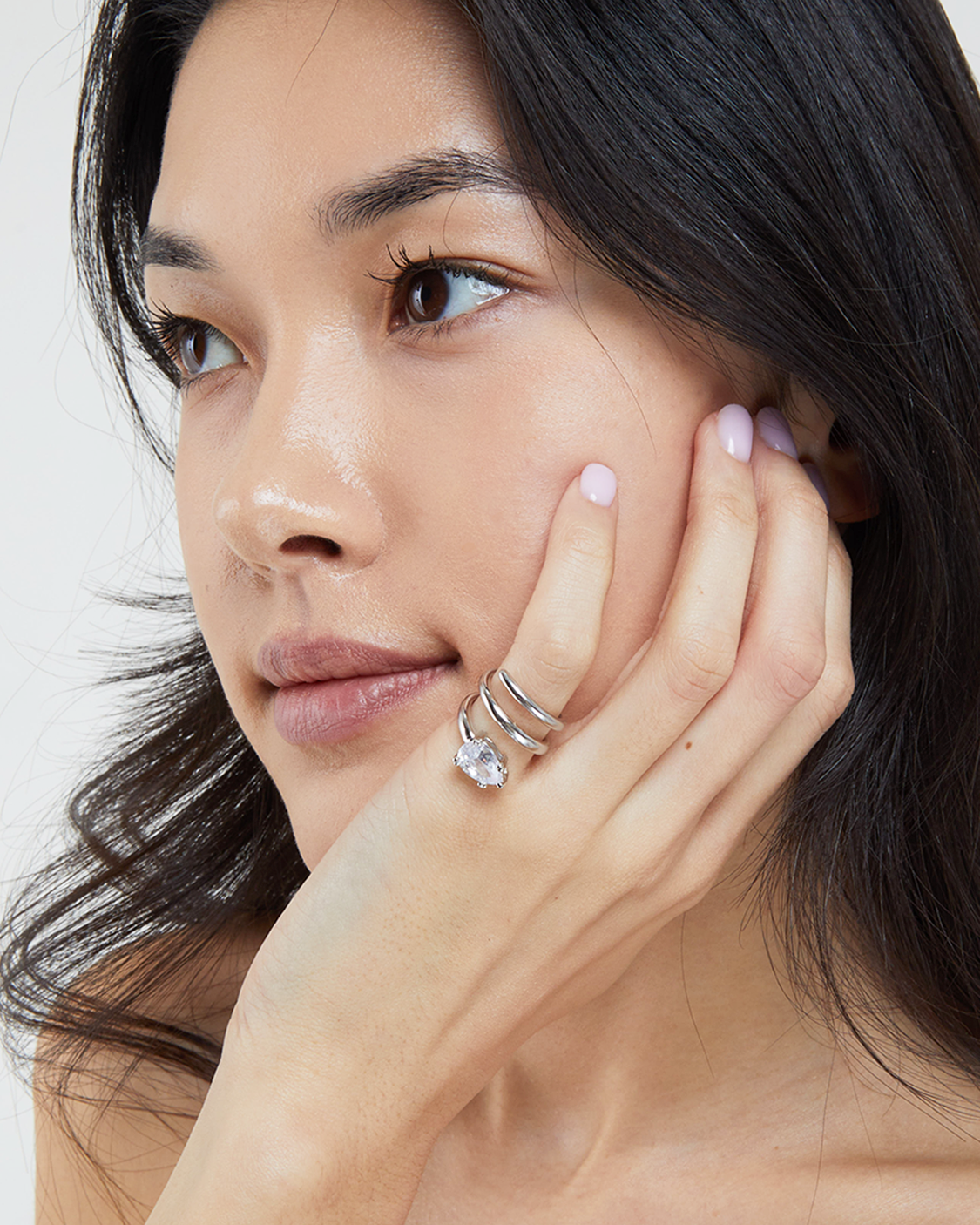 Woman with dark hair and silver rings on her fingers against a neutral background