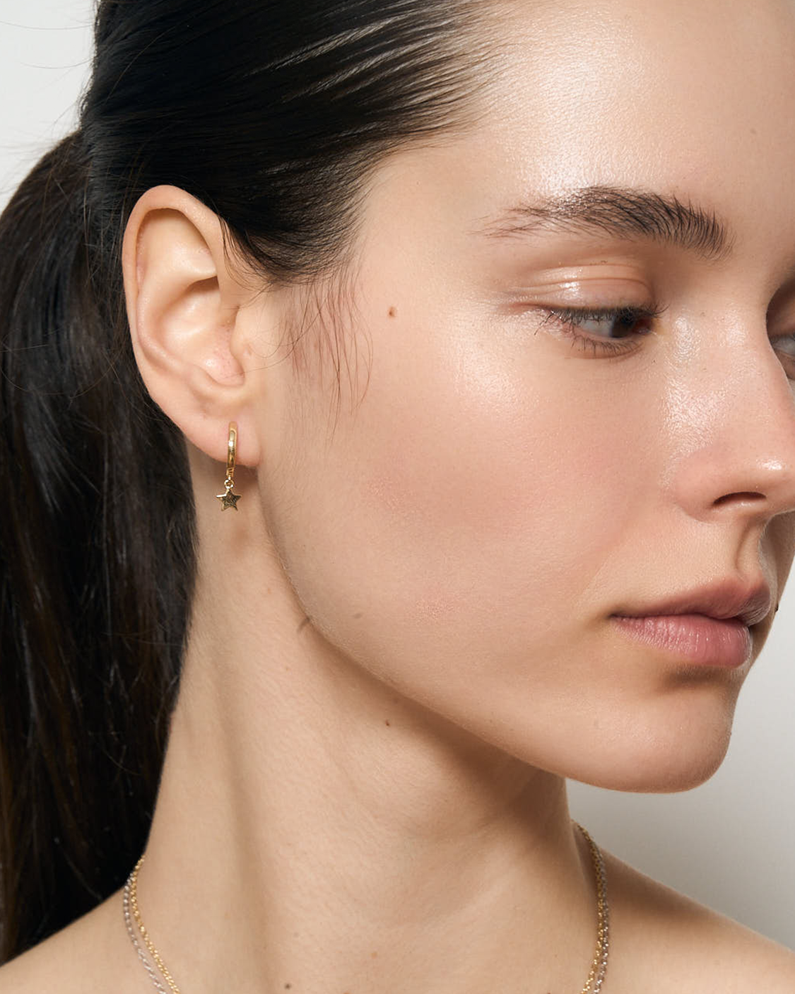 Close-up of a woman's face with a gold star-shaped hoop earring on a neutral background