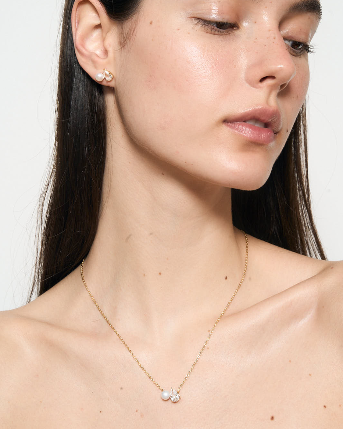 Close-up of a woman wearing a gold necklace with a white pendant 