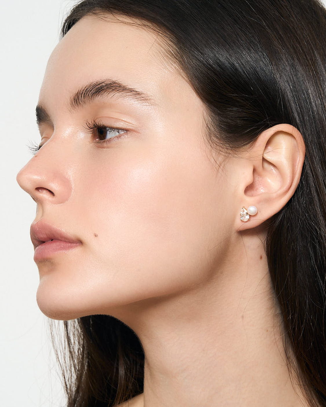 Close-up of a woman's side profile with a focus on her ear wearing white earrings.